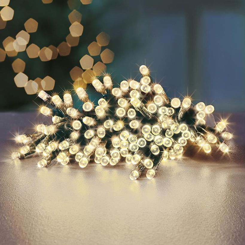 Battery-operated LED fairy lights with 24 warm white bulbs coiled on a light surface, featuring a timer function, displayed against a blurred background with decorative bokeh lights