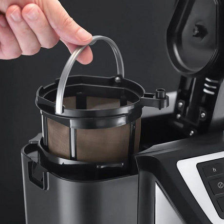Hand lifting stainless steel filter basket with brown coffee grounds from black Russell Hobbs Victory Grind and Brew coffee machine showing drip coffee maker design with silver accents