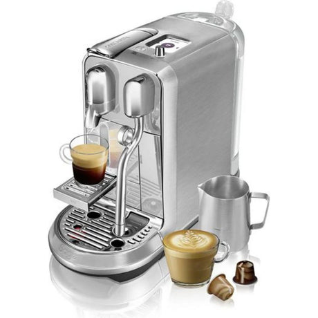 Sage Nespresso Creatista Plus stainless steel coffee machine dispensing espresso into glass cup with milk frother, cappuccino cup and coffee capsules displayed alongside