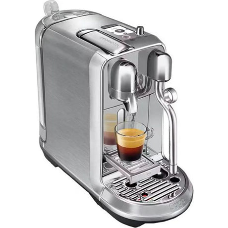 Sage Nespresso Creatista Plus stainless steel coffee machine dispensing espresso into glass cup with chrome steam wand and drip tray visible