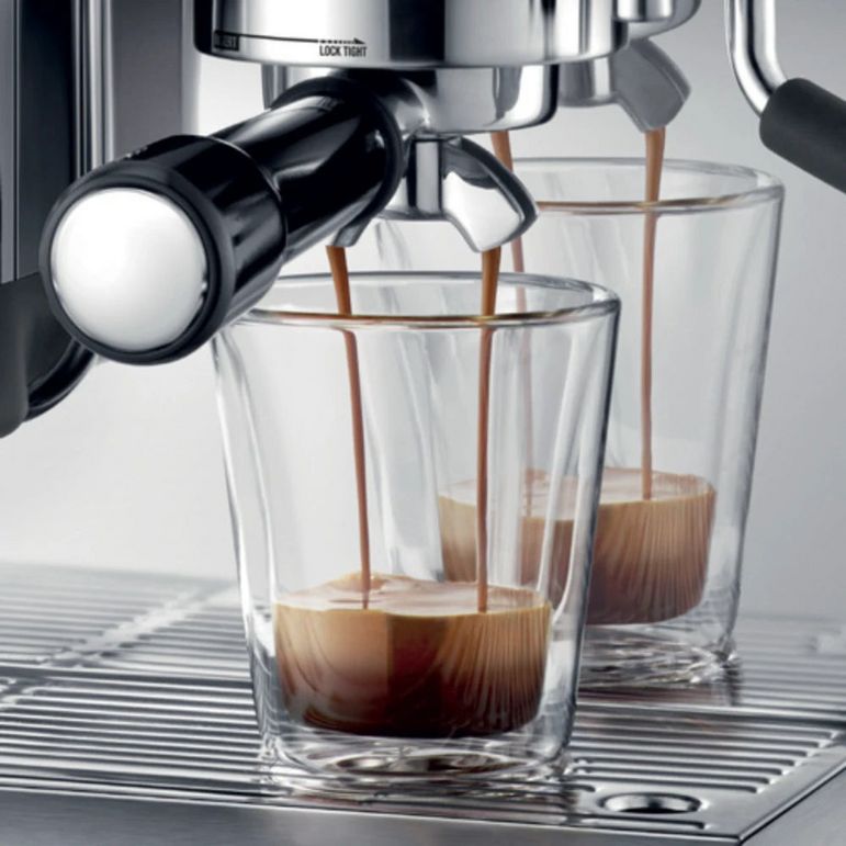 Sage Barista Express Impress black espresso machine dispensing dark coffee into clear glass cups on a drip tray, showing the portafilter and dual shot glasses mid-pour