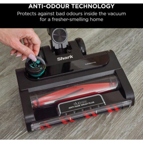 Shark vacuum anti-odour technology cartridge being inserted into black vacuum cleaner head showing turquoise circular filter and red anti hair wrap plus technology on wooden floor