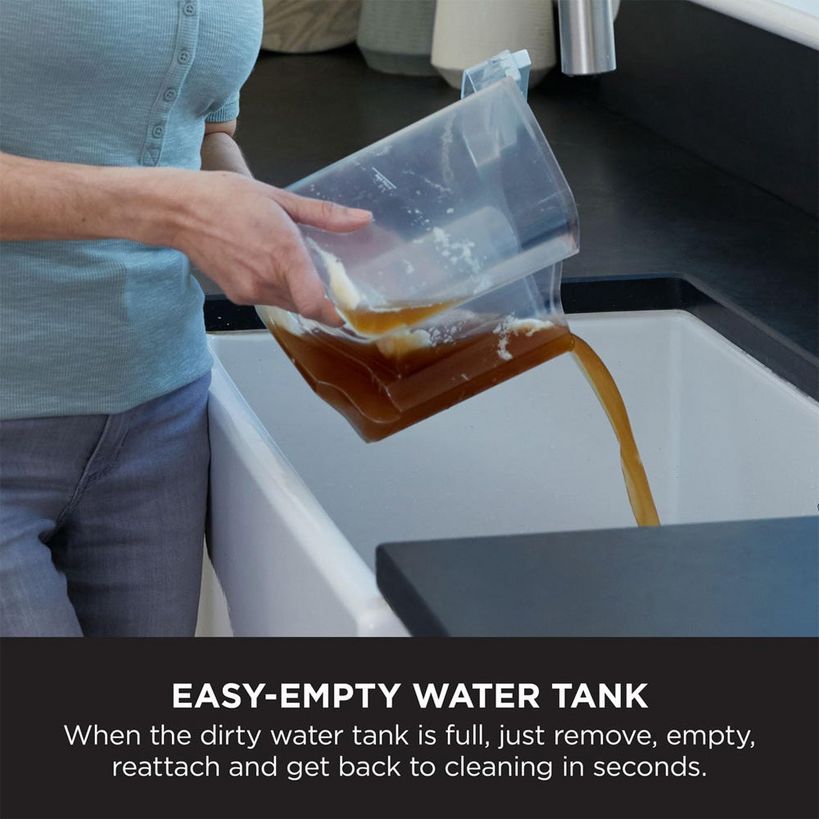 Person in light blue cardigan emptying brown dirty water from transparent tank of Shark CarpetXpert carpet cleaner into white basin, demonstrating easy-empty water tank feature