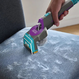 Shark CarpetXpert HairPro Pet deep carpet cleaner with purple and teal coloring being used on light blue upholstered furniture, showing the built-in StainStriker feature in action removing stains