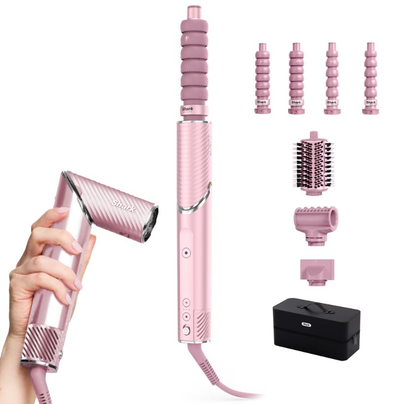 A pink cordless hair styling tool set shown on a white background, including the main wand, a hand holding the wand, several attachment heads, a brush, a nozzle, a small accessory piece, and a black storage case.