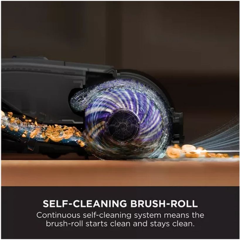 Close-up product demonstration of Shark HydroVac self-cleaning brush roll showing purple spiral motion and debris ejection with text describing continuous self-cleaning system