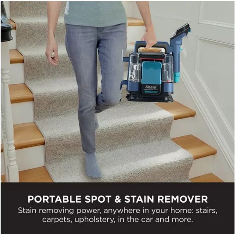 Woman in grey jeans using Shark StainStriker portable spot and stain remover on beige carpet-covered stairs with wooden treads in a white-walled home interior