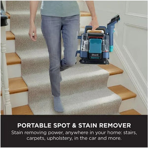 Woman in grey jeans using Shark StainStriker portable spot and stain remover on beige carpet-covered stairs with wooden treads in a white-walled home interior