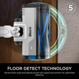 Shark PowerPro cordless stick vacuum cleaner in white and black with transparent dust bin, shown from above on wooden and carpeted flooring, featuring Floor Detect Technology diagram with 5 year guarantee badge