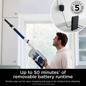 Man using blue and white Shark PowerPro cordless stick vacuum to clean near window, with inset showing removable battery pack being charged on wall outlet and 5 year guarantee badge, highlighting up to 50 minutes battery runtime in ECO mode