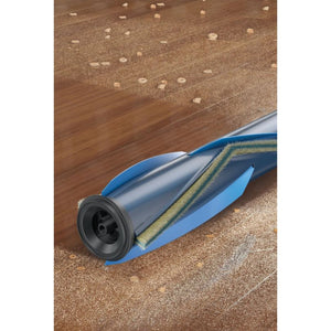Shark PowerPro Cordless Stick Vacuum IZ380UK with blue body and motorized brush head shown on cork and wooden floor with scattered crumbs and pet hair