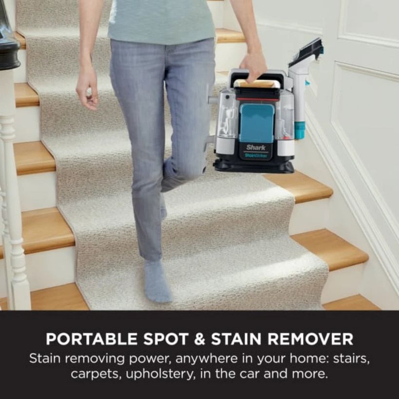 Woman in blue t-shirt and grey jeans carrying white and teal Shark StainStriker portable spot and stain remover down carpeted stairs with wooden treads in a home interior