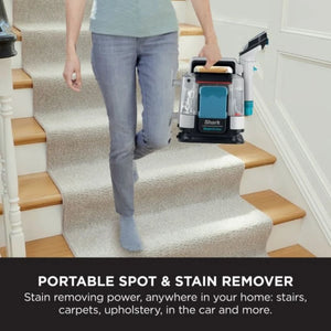 Woman in blue t-shirt and grey jeans carrying white and teal Shark StainStriker portable spot and stain remover down carpeted stairs with wooden treads in a home interior