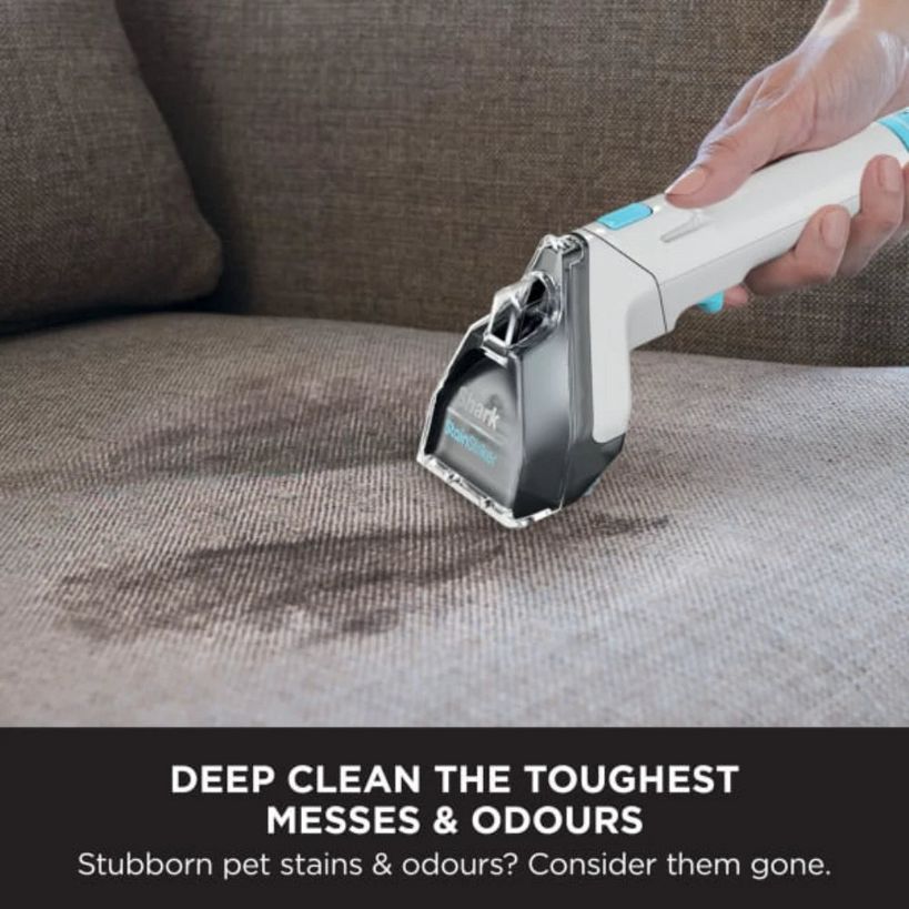 Shark StainStriker Pet Stain & Spot Cleaner being used on beige upholstered sofa to remove pet stains, white and grey handheld cleaning device with blue accents in action