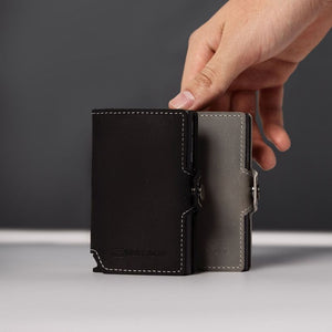 Hand holding Wallet Junkie Pro Slim midnight black leather card wallet with white stitching, displaying compact minimalist design for up to 9 cards against gray background