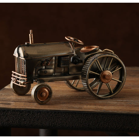 Vintage-style metal tractor ornament with bronze and brass patina finish, featuring detailed wheels, steering wheel, and exhaust pipe, displayed on wooden surface against dark background