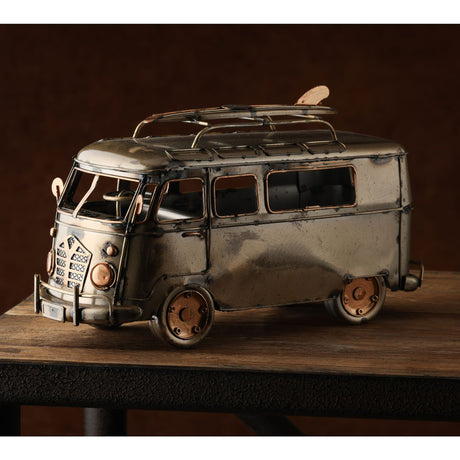 Vintage metal campervan ornament with silver and bronze finish, featuring detailed windows, roof rack with surfboard, and weathered patina, displayed on wooden surface against dark background