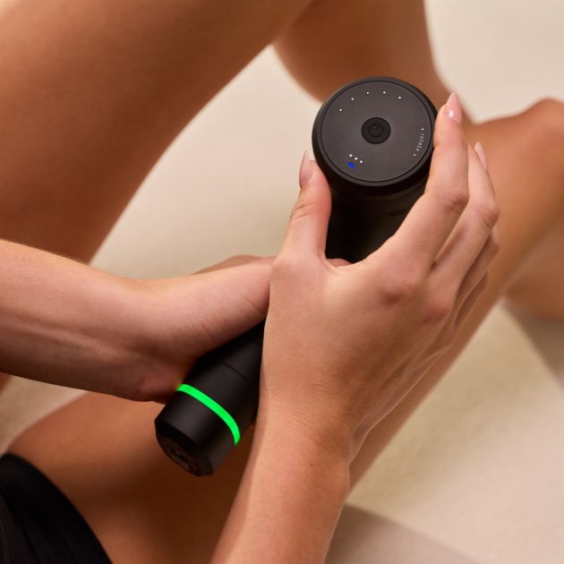 Person holding black Hyperice Hypervolt 3 massage gun with glowing green accent band and blue LED indicator lights on top