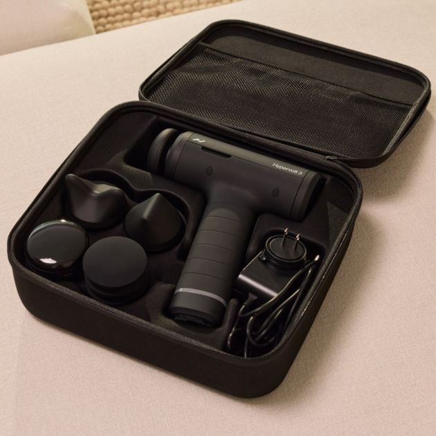Hyperice Hypervolt 3 massage gun in black with carrying case showing device, multiple attachment heads, charging cable and accessories on white surface