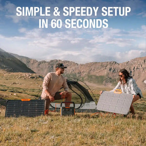 Two people setting up a portable solar power system in a mountainous valley, with a Jackery portable power station connected to multiple foldable solar panels including the SolarSaga 80W panel, demonstrating quick outdoor camping setup