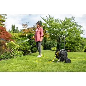 Woman in pink shirt using a Karcher black and yellow hose trolley with 20 metre yellow hose in a lush green garden with trees and flowering shrubs