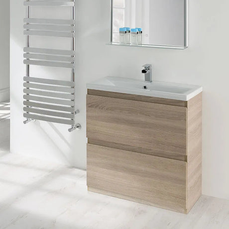 Modern bathroom vanity unit with Nebraska Oak wood finish featuring two drawers, white ceramic sink, chrome tap and mirror cabinet above, paired with silver heated towel rail on white marble-effect flooring
