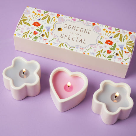 Three lit candles in flower-shaped holders with a decorative box on a purple background