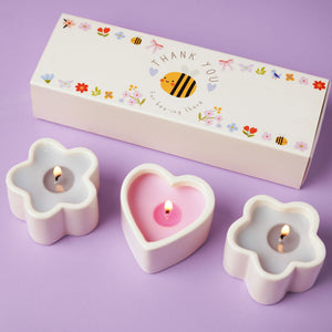Three flower-shaped candles with a 'Thank You' box on a purple background