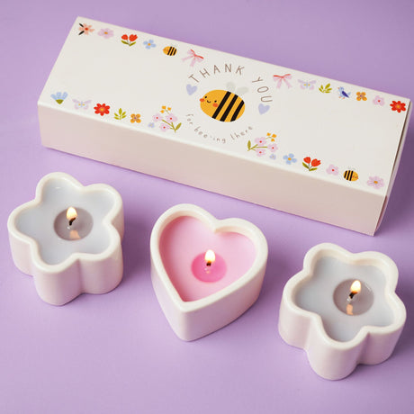 Three flower-shaped candles with a 'Thank You' box on a purple background