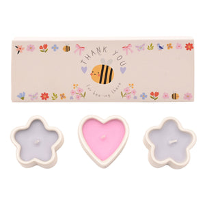 Set of three decorative mini candles in flower and heart shapes with cream-colored wax containers, featuring pink heart-shaped candle in center and lavender flower-shaped candles on sides, accompanied by beige gift box decorated with colorful illustrated bee and floral motifs and Thank You message