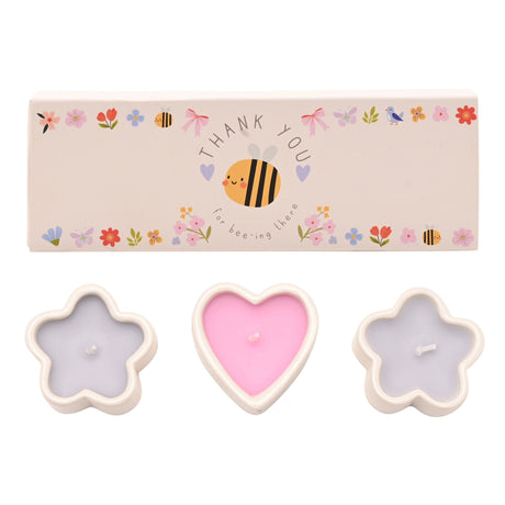 Set of three decorative mini candles in flower and heart shapes with cream-colored wax containers, featuring pink heart-shaped candle in center and lavender flower-shaped candles on sides, accompanied by beige gift box decorated with colorful illustrated bee and floral motifs and Thank You message