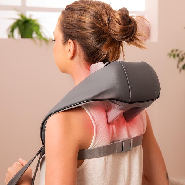 Woman using a handheld massager on her back in a home setting