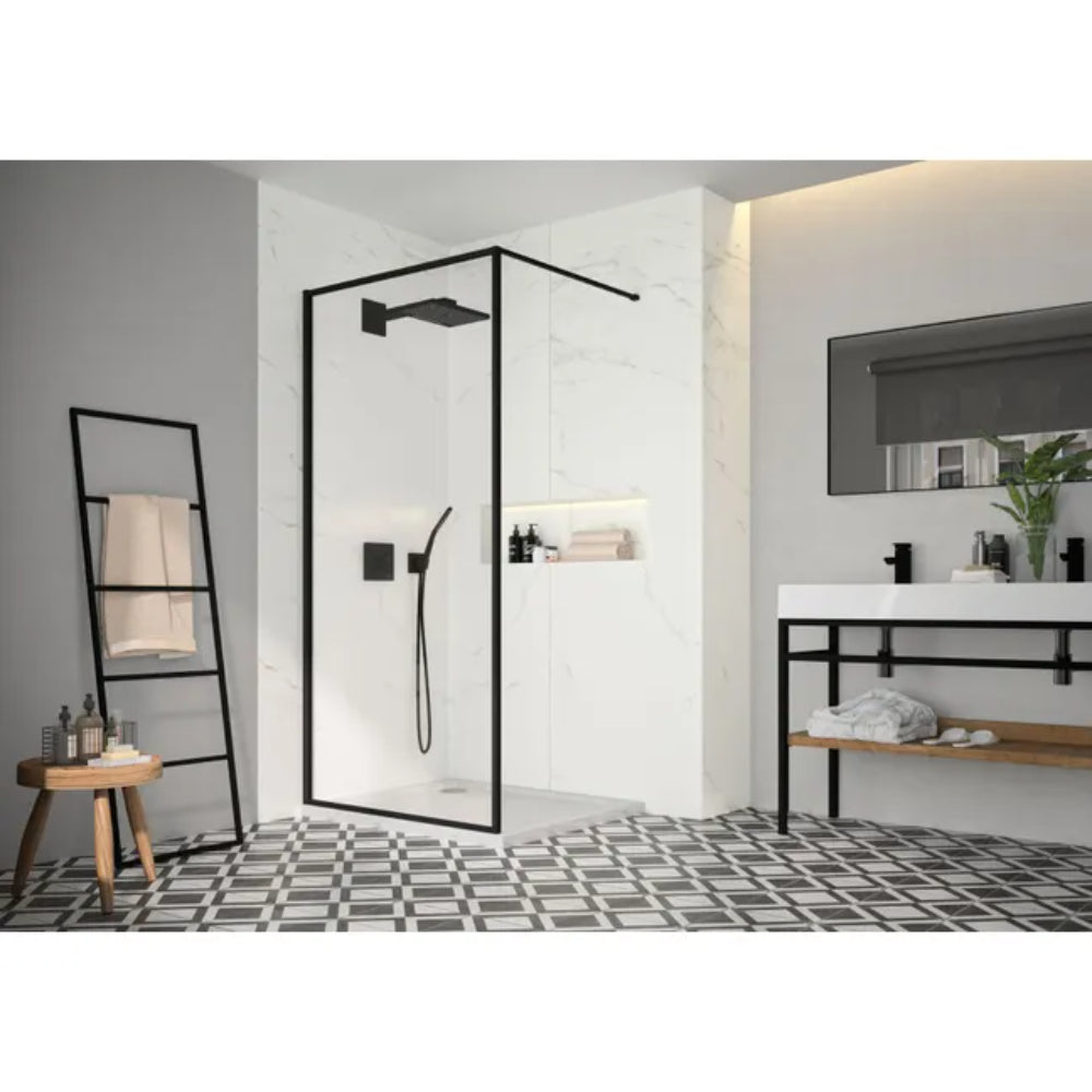 Modern bathroom featuring Merlyn 6 Series Sleek framed wetroom panel with matt black frame and clear glass, white marble tiling, black and white geometric floor pattern, white vanity sink with mirror, wooden ladder towel rack, and contemporary fixtures
