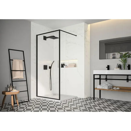 Modern bathroom featuring Merlyn 6 Series Sleek framed wetroom panel with matt black frame and clear glass, white marble tiling, black and white geometric floor pattern, white vanity sink with mirror, wooden ladder towel rack, and contemporary fixtures