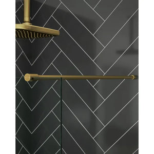 Merlyn 8mm wetroom panel in brushed brass finish with matching showerhead and towel rail against herringbone patterned black subway tiles