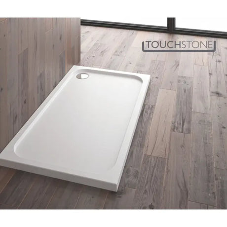 White rectangular shower tray with curved corners on grey wood-effect bathroom flooring, Merlyn Touchstone branding visible on wall behind