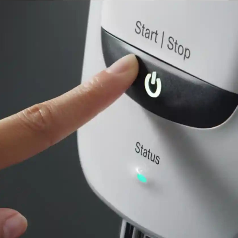 Hand pressing a 'Start/Stop' button on an appliance with a dark background