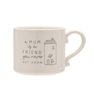 Cream ceramic mug with grey text and illustrations reading "a MUM is a FRIEND you never OUT GROW" alongside a simple line drawing of a house with a flower, featuring a curved handle
