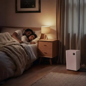 White Masterplug Puredry SmartEnergy dehumidifier air purifier positioned on wooden floor in modern bedroom next to bed with couple sleeping and bedside lamp