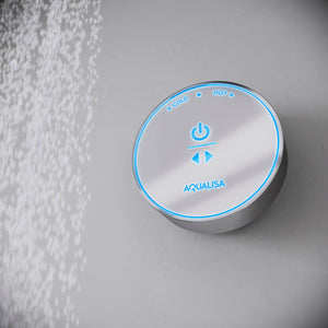 Aqualisa Quartz Blue digital shower controller mounted on white textured wall, featuring circular brushed metal face with blue LED ring, power button, temperature controls marked Cold and Hot, and down arrow adjustment buttons
