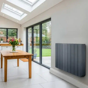Grey vertical oil filled wall-mounted radiator in modern kitchen extension with skylights, wooden dining table and black framed glass doors overlooking garden