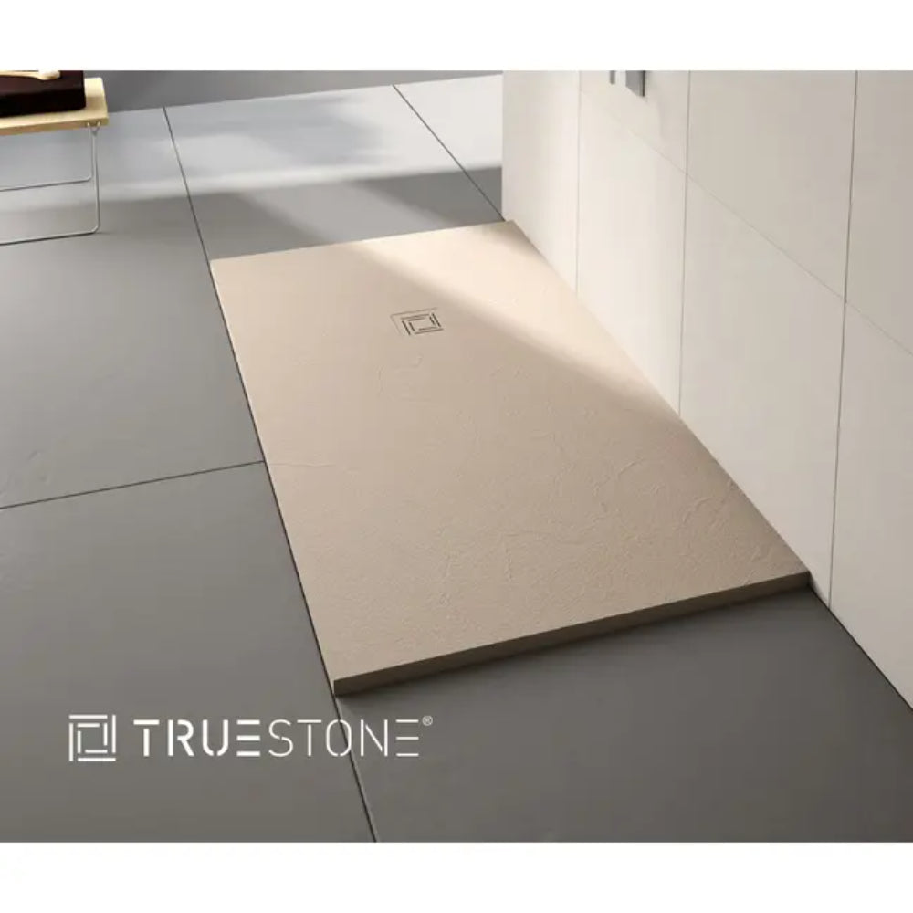 Merlyn TrueStone rectangular shower tray in cream beige with integrated drain, installed in modern white tiled bathroom with grey floor