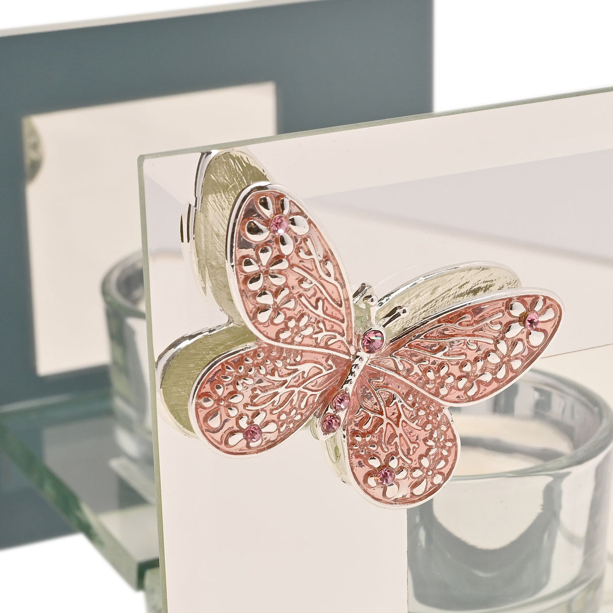 Pink and gold filigree butterfly glass tea light holder with intricate cut-out wing details and pink crystal accents, displayed on white card with blurred interior decor background