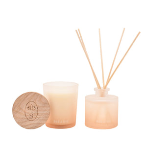 Serenity Breathe Diffuser and Candle Set featuring a wooden-lidded frosted glass candle with peachy gradient wax, matching reed diffuser with natural wooden sticks, and engraved lotus logo on circular wood lid against white background