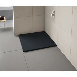 Modern bathroom shower enclosure featuring a black rectangular Merlyn Truestone shower tray with integrated waste, installed on light grey floor tiles with cream tiled walls and chrome mixer tap visible