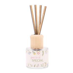 Reed diffuser with wooden sticks in a clear glass bottle decorated with colorful wildflower illustrations and pink text reading "you're so SPECIAL" with natural wood cap