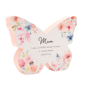 Butterfly-shaped floral mantelpiece decoration in soft pink and cream with watercolor flowers featuring pink peonies and blue blooms, text reading "Mum I am a STRONG woman because a strong woman RAISED me" with a bee detail, ideal for Mother's Day gifts