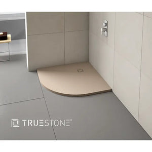 Merlyn Truestone beige curved shower tray with integrated drain in modern bathroom with grey and cream wall tiles and chrome fixtures