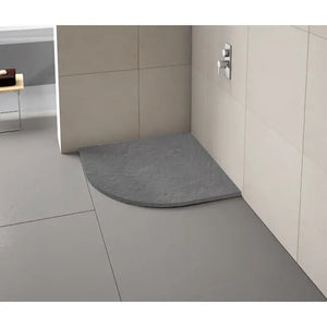 Modern grey curved quadrant shower tray installed in minimalist bathroom with light grey large format tiles and beige wall panels, chrome valve visible
