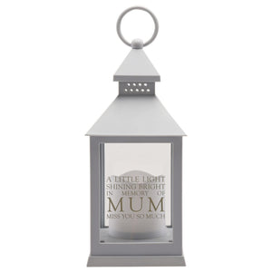 Grey metal graveside lantern with conical roof and ring handle, featuring a frosted white candle inside behind clear glass panels, engraved with "A little light shining bright in memory of MUM Miss you so much" text in grey lettering